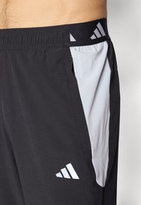 Zwarte sportshorts met een lichtgrijs zijpaneel, elastische tailleband en witte logo-accenten. Gemaakt van lichtgewicht, ademend materiaal.