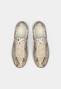 Ζευγάρι μπεζ αθλητικά παπούτσια με σχέδιο φίδι και μπεζ κορδόνια, σε θέα από πάνω πάνω σε απλό γκρι ανοιχτό φόντο.