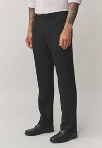 Pantaloni formali neri con design sartoriale, fronte piatto, tasche laterali e texture liscia, abbinati a mocassini neri.