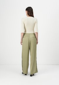 Beige fitted ribbed sweater with elbow-length sleeves paired with wide-leg olive green trousers featuring side slits and back pockets.