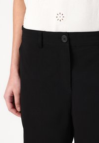 Pantalon noir au tissu lisse, avec une fermeture à bouton et des passants de ceinture. La taille est conçue pour un ajustement confortable.