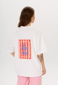 Witte oversized t-shirt met een levendige grafische afbeelding met de titel "La Dolce Vita" op de rug, met een rood-wit gestreepte achtergrond en blauwe tekst.