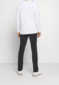 Vit långärmad skjorta i kombination med svarta byxor med siddragkedjor. Sneakers i vitt med grå sulor, vilket framhäver en avslappnad stil.