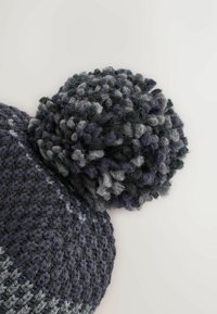 Knit beanie in dark navy and gray tones, featuring a large textured pom-pom on top. Ribbed design with a cozy texture.
