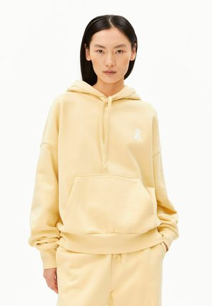 Gele oversized hoodie gemaakt van zacht stof, voorzien van een kangoeroezak en een capuchon met trekkoord. Versierd met een klein wit logo.