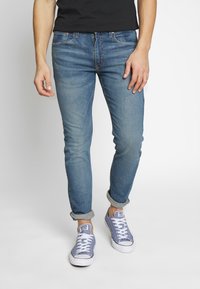 Hellblaue Denimjeans mit schmal zulaufender Passform, aufgekrempelten Bündchen, klassischem Fünf-Taschen-Design und dezenten Verwaschungseffekten. Kombiniert mit grauen Sneakern.