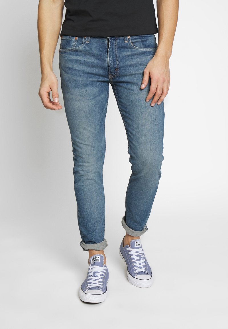 Hellblaue Denimjeans mit schmal zulaufender Passform, aufgekrempelten Bündchen, klassischem Fünf-Taschen-Design und dezenten Verwaschungseffekten. Kombiniert mit grauen Sneakern.