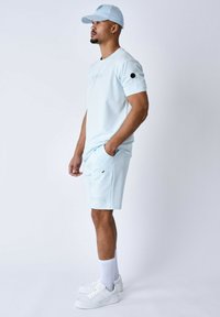 Lichtblauw sportoutfit met een shirt met korte mouwen en bijpassende shorts. Inclusief zakken en geborduurde details. Draagt met witte sneakers.