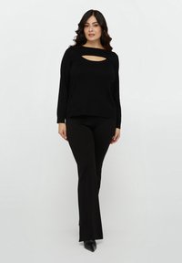 Musta neulepaita, jossa on pyöreä kaula-aukko ja vaakasuuntainen leikkauskuvio. Yhdistetty mustiin slim fit -housuihin ja teräväkärkisiin mustiin kenkiin.