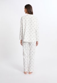 Leichtes, langärmliges Pyjama-Set in Creme mit kleinen grauen Herzmustern. Weicher Stoff mit geraden Hosen und einer entspannten Passform.