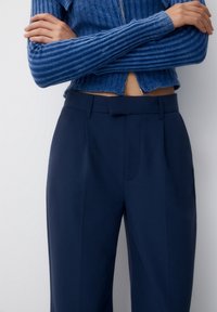 Námornické kalhoty s rovnými nohavicemi, vybavené předními sklady a plochým pasem. V kombinaci s modrým svetrem se žebrovaným vzorem a zkrácenou délkou.