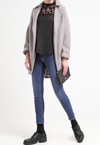 Manteau en laine gris porté sur un top en dentelle noir, associé à un jean slim bleu et des chaussures à lacets noires. Accessoirisé avec une pochette noire.