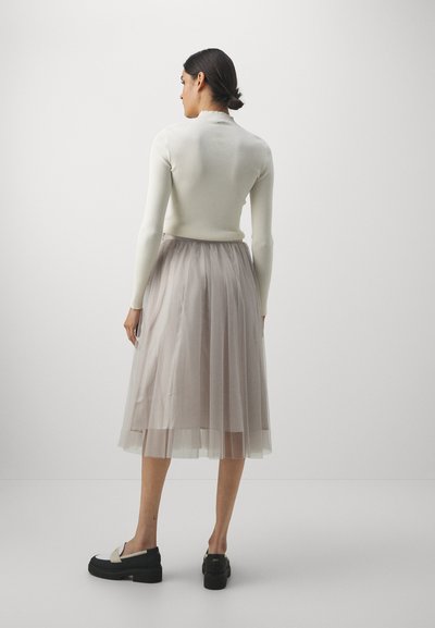 Top bianco a maniche lunghe a coste abbinato a una gonna in tulle grigia chiara, lunga fino al ginocchio. Scarpe platform nere con un accento color crema.