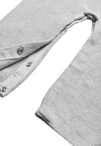 Indumento grigio a maglia con tessuto testurizzato, dotato di chiusure a pressione sui lati e polsini a coste. Il design include un'apertura rotonda per la testa.