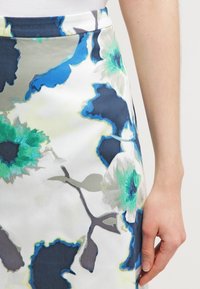 Květinová tužková sukně se modrými a zelenými květy na bílém pozadí. Hladká látka s přiléhavým pasem a elegantním střihem.