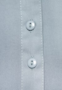 Detailní záběr na světle modrou látku s dvěma bílými knoflíky, viditelnými švy a hladkým, strukturovaným tkaním.