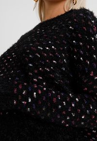 Czarny, puszysty sweter z wielokolorowymi nitkami w czerwonym, białym i niebieskim kolorze, o teksturowanym splocie i szerokich rękawach.