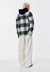 Crno-bijela flanelasta košulja na kockice s mekom teksturom, nošena preko crne hoodice; uparena s širokim kremastim hlačama.