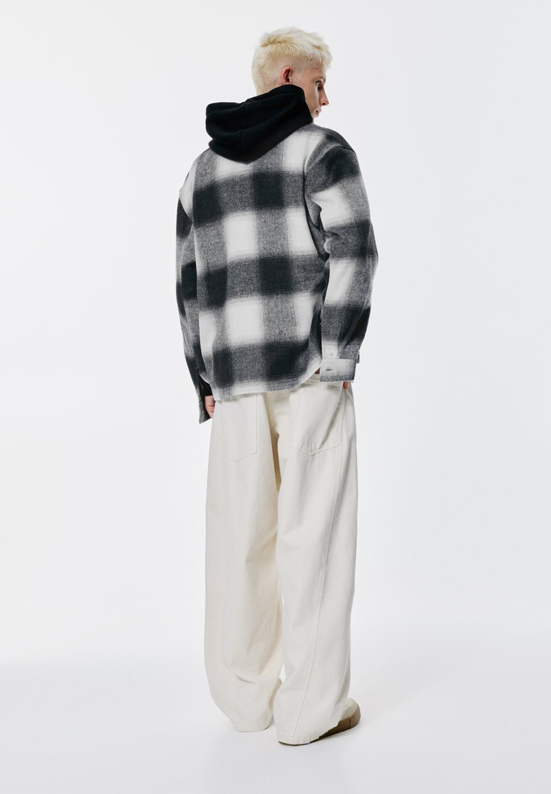 Crno-bijela flanelasta košulja na kockice s mekom teksturom, nošena preko crne hoodice; uparena s širokim kremastim hlačama.