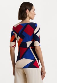 Top ajustado de manga corta con un colorido patrón geométrico que presenta formas rojas, azules y beiges sobre un fondo navy. Tela de mezcla de algodón.