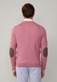 Maglione rosa con collo rotondo e toppe marroni sui gomiti. Realizzato in tessuto morbido, presenta un design aderente e polsini e orlo a coste.