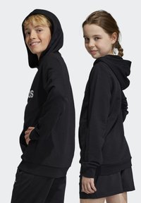 Sudaderas con capucha negras y bolsillos delanteros, con una textura suave y un corte holgado. El diseño incluye un logo blanco en la parte delantera.