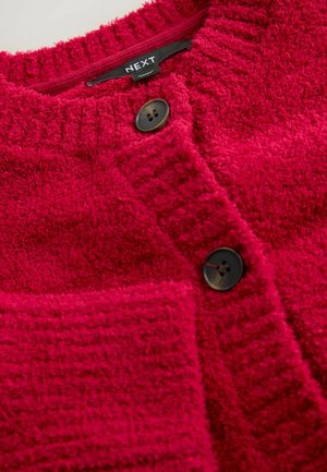 Miękki czerwony kardigan z prążkowanym kołnierzem, dwoma czarnymi guzikami i teksturowaną powierzchnią. Z prawej strony z przodu znajduje się kieszeń.