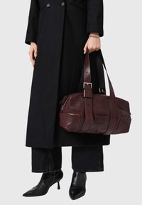 Burgundy leather handbag with a rectangular shape, top zip closure, adjustable, wide strap, and visible stitching details.