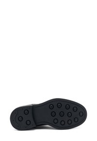Suola di scarpa in gomma nera con una forma curvata, caratterizzata da numerosi battistrada circolari per una migliore aderenza. Esterno liscio con dettagli laterali ben definiti.