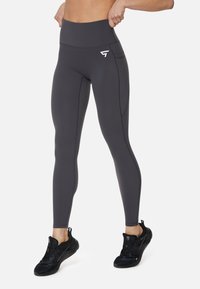 Hoge taille, donkergrijze leggings van rekbare stof, met een zijzak en witte logo-details, aangevuld met zwarte hardloopschoenen.