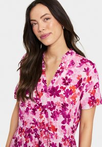 Rochie florală în nuanțe de roz și violet, cu mâneci scurte, decolteu în V și o tivă evazată cu o textură gathered.