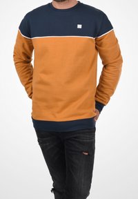 Sweat-shirt bicolore avec une partie supérieure bleu marine et une partie inférieure orange. Tissu doux, poignets côtelés et bande blanche en accent.