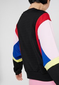 Mustapaita, jossa on moniväriset hihnat punaisena, vaaleanpunaisena, sinisenä ja keltaisena. Ribattuja hihansuita ja kaula-aukko, pehmeä rakenne ja rento muotoilu.