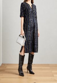 Mörkblå paljettklänning med vertikala ränder, korta ärmar och knappstängning. Matchad med svarta knähöga stövlar och en silverhandväska.