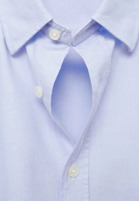 Chemise à col bleu clair en tissu, dotée d'une patte de boutonnage étroite avec des boutons blancs et une texture subtile sur la surface du tissu.
