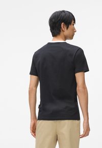 Černé bavlněné tričko s krátkým rukávem, kulatým výstřihem a božním štítkem. Tkanina vypadá hladce, má jednotnou barvu a žádné viditelné vzory.