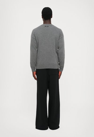 Grau gestrickter Pullover mit rundem Halsausschnitt, gerippten Bündchen und Saum. Kombiniert mit weiten schwarzen Hosen. Rückansicht.
