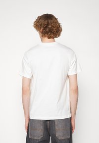 Valkoinen puuvillainen t-paita lyhyillä hihoilla, pyöreällä kaula-aukolla ja rentoa istuvuutta; takana on puhdas pinta ilman grafiikoita tai koristeita.