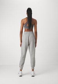 Woman with long hair in a high ponytail wears a gray sports bra, gray sweatpants, and white sneakers, standing against a plain white background.