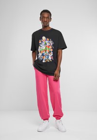Sort grafisk t-shirt med farverige tegneseriefigurer, parret med løstsiddende lyserøde sweatpants og hvide sneakers.