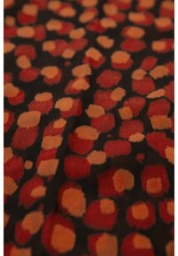 Tkanina o ciemnym tle z wzorem dużych, nieregularnych plam w kolorach czerwonym i pomarańczowym, przedstawiająca miękki, teksturowany materiał.