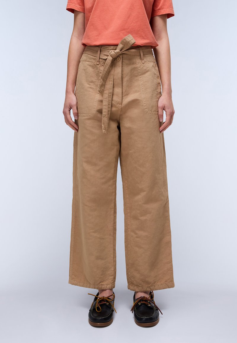 Beige wijde broek met een riem, gemaakt van een gladde katoenstof. Beschikt over zijzakken en zichtbare stikdetails. Zwarte schoenen.