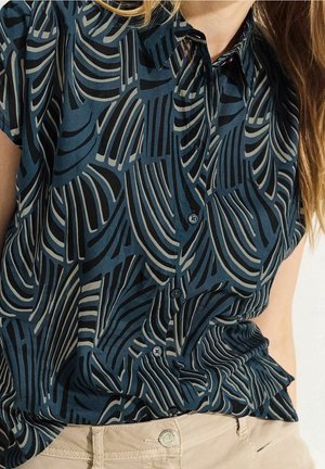 Blusa a maniche corte in tessuto blu scuro con motivo a onde grigie e nere. Chiusura con bottoni e vestibilità comoda.