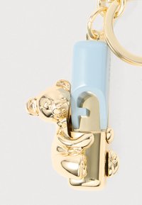 Breloc în ton auriu, având un brichetă de plastic albastru însoțită de o figurină de urs care îl îmbrățișează. Ursul are un finisaj lucios și trăsături faciale detaliate.