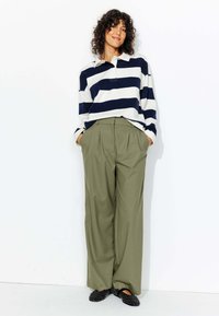 Polo rayé à manches longues bleu marine et blanc, pantalon large olive, et ballerines noires avec des motifs circulaires.