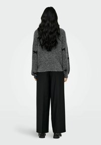 Grijze gebreide trui met een losse pasvorm en verlaagde schouders, gecombineerd met zwart hoge taille wijde broek en zwarte enkellaarsjes.