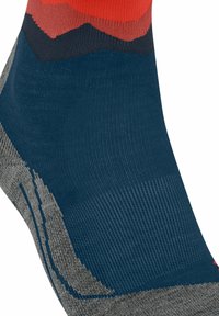 Primo piano di una calza multicolore con motivi in maglia rossa, nera, blu navy e grigia, con dettagli di tessuto testurizzato.