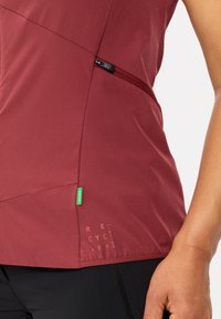 Top senza maniche color rubino realizzato in materiale riciclato, con tasca con zip, pannelli testurizzati e etichetta verde che indica la sostenibilità.