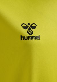 Jasnożółta tkanina o teksturowanym wykończeniu z czarnym logo stylizowanej pszczoły oraz nazwą marki "hummel" poniżej.