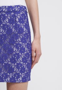 Falda de encaje morado con patrón floral, que presenta un diseño ajustado y una cinturilla suave. La superposición de encaje texturizado añade interés visual.